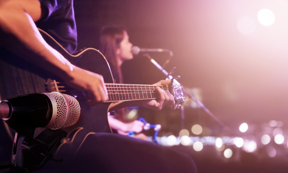 Image showing guitar player and microphone with sun flare in the background. 